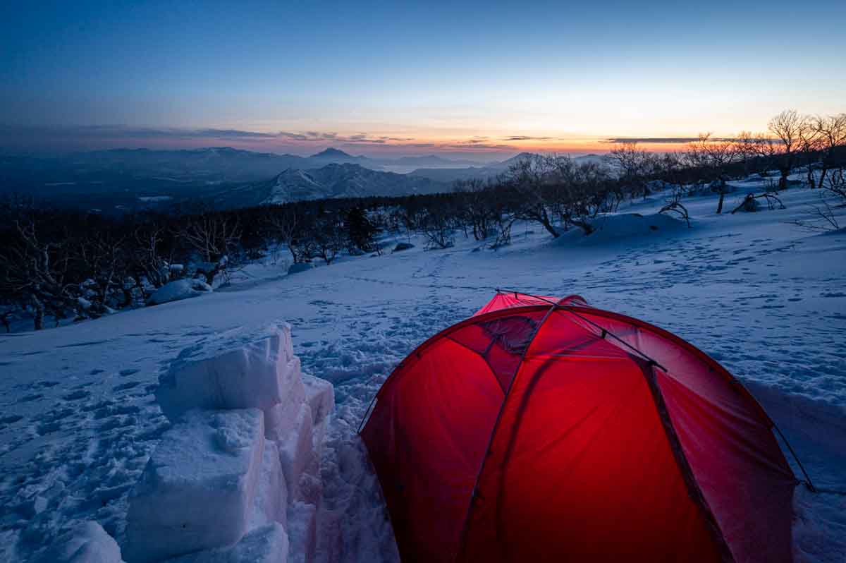 雪山で日の出前の空とテントを撮影